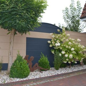 Im Garten steht eine elegante Figur, umgeben von üppigem Grün und weißen Blumen, die eine ruhige Atmosphäre schafft.
