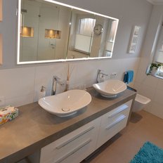Ein modernes Badezimmer mit zwei eleganten Waschbecken und einem großen Spiegel, der den Raum hell erleuchtet.