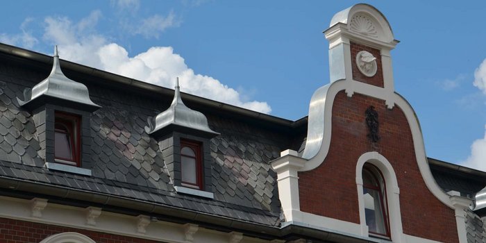 Die detailreiche Dachkonstruktion zeigt elegante Erkerfenster und geschwungene Ziegel, die den historischen Charme betonen.