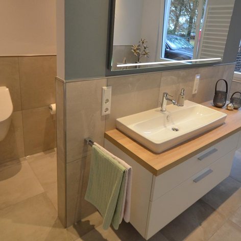 Ein helles Badezimmer mit einem minimalistischen Design, das ein Waschbecken, einen Spiegel und eine Toilette umfasst.