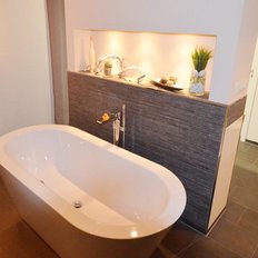 Ein modernes Badezimmer mit einer freistehenden Badewanne, eleganten Wandleuchten und stilvollen Dekorationen auf dem Regal.