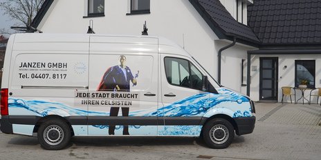 Ein Lieferwagen mit auffälliger Werbung steht vor einem modernen Haus, umgeben von einem gepflegten Garten.