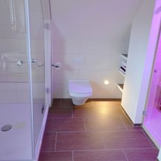 Ein modernes Badezimmer mit einer gläsernen Dusche, einem WC und einem Zugang zu einer Sauna mit sanftem, pinkem Licht.